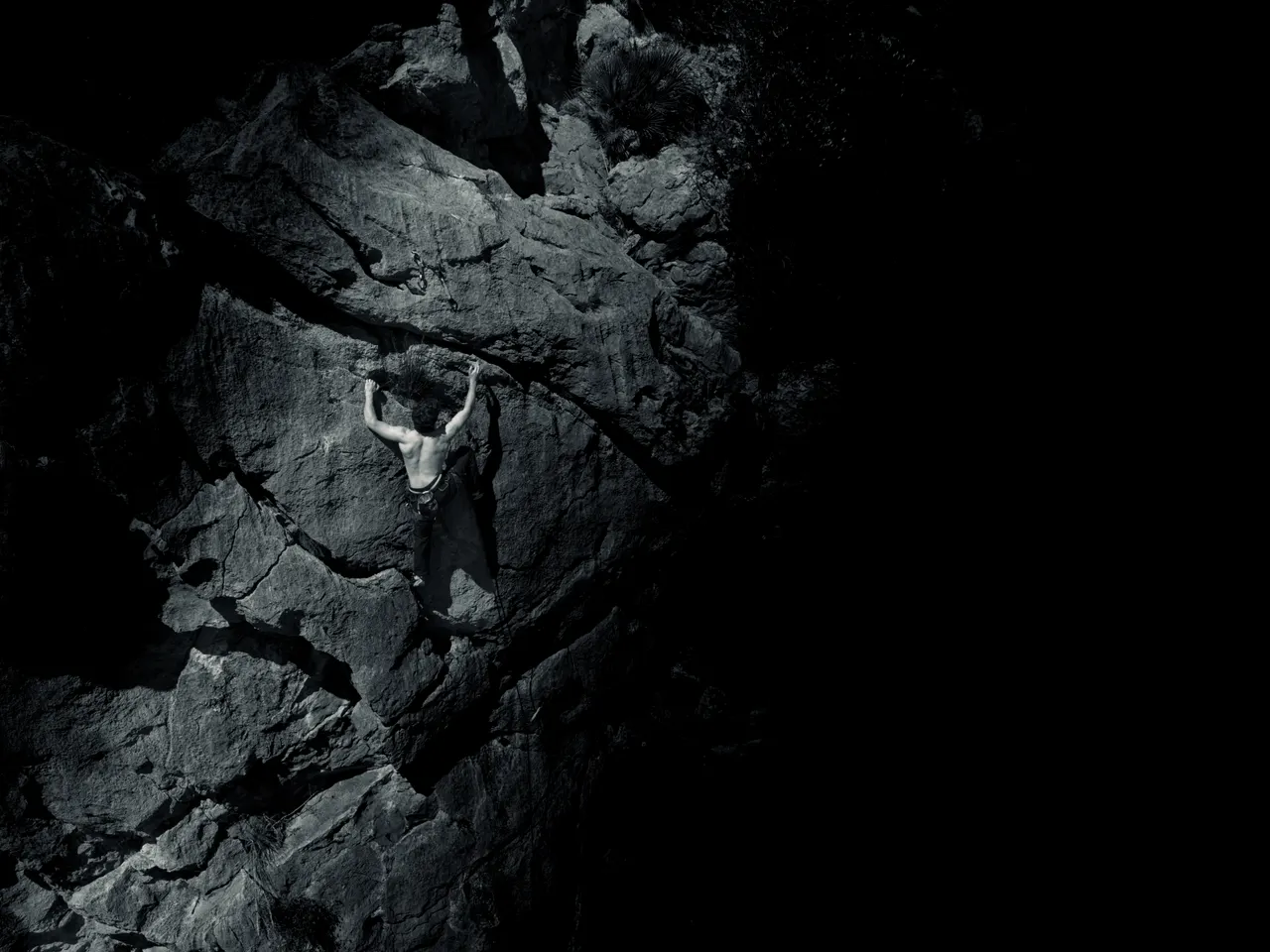Escalador en una paret de roca fosca, en blanc i negre.
